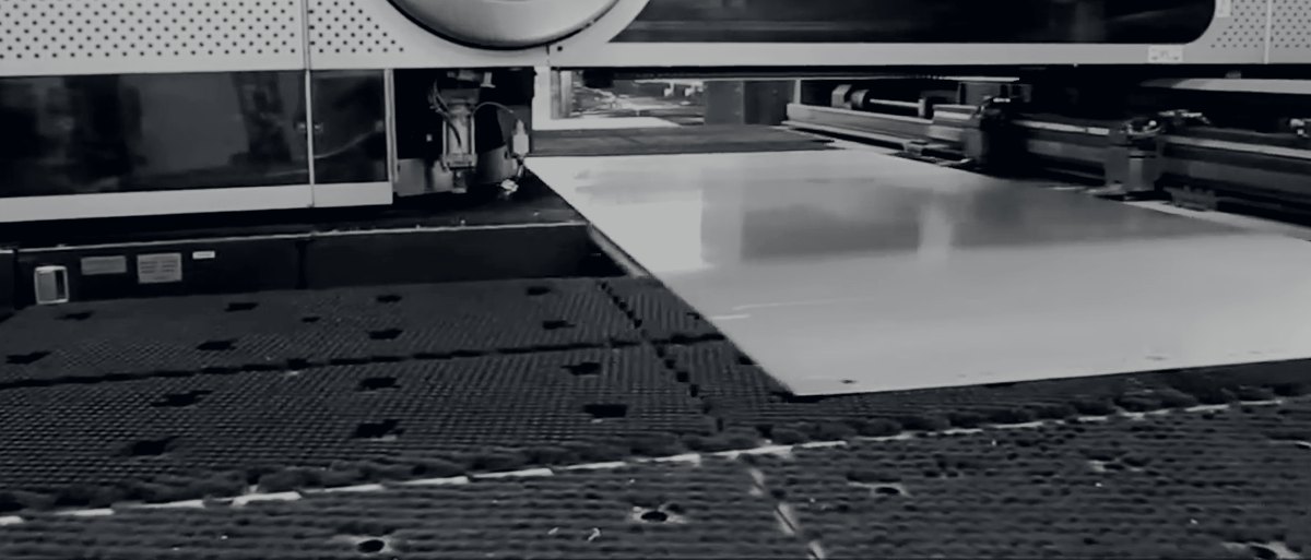 An aluminium panel on the bed of a combination laser and punch press
